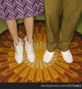Close-up of Caucasian mid-adult male and female legs in vintage clothing against sunburst rug.