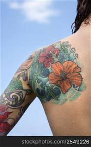 Close-up of Caucasian woman&acute;s back and shoulder covered with floral tattoos.