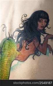 Close-up of Caucasian woman&acute;s back with mermaid tattoo.