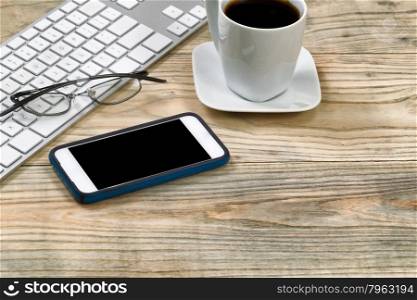 Close up of cell phone, reading glasses, keyboard and dark coffee on rustic desktop.