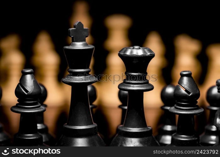 Close up of Chess pieces on a reflective mirror board surface with a plain black background