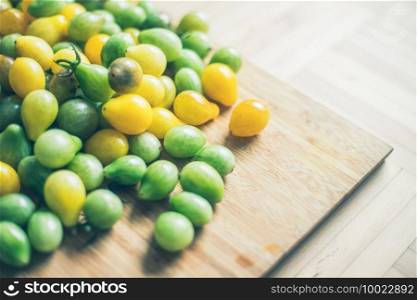 Close up of cocktail tomatoes on wooden plate, yellow and green