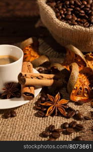 Close-up of coffee cup with cinnamon, star anise, dried orange fruit and a coffee sack on background