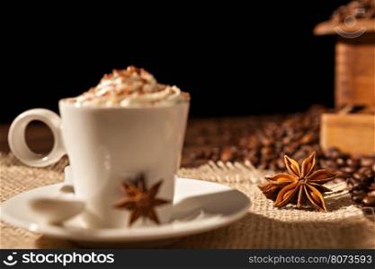 Close-up of coffee cup with whipped cream and star anise on a black background. Close-up of coffee cup with whipped cream and star anise