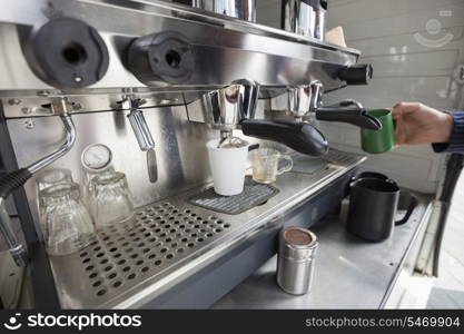 Close-up of coffee machine with hand holding cup