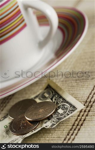 Close-up of coins on an American one dollar note beside a tea cup
