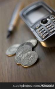 Close-up of coins with a mobile phone and a pen on the table