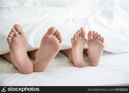 Close up of couple barefoot under blanket in bedroom in honeymoon vacation holiday in long weekend at home. Relaxation of sexual and romantic people after wedding ceremony. Valentines day love theme.