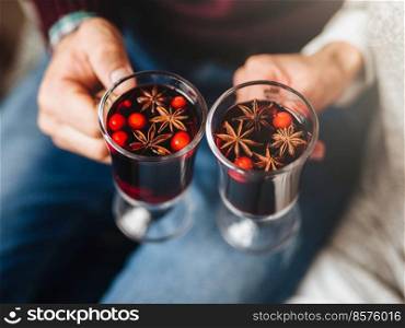 Close-up of crop couple holding hot mulled wine with spices served in glasses. . Crop people holding warm punch