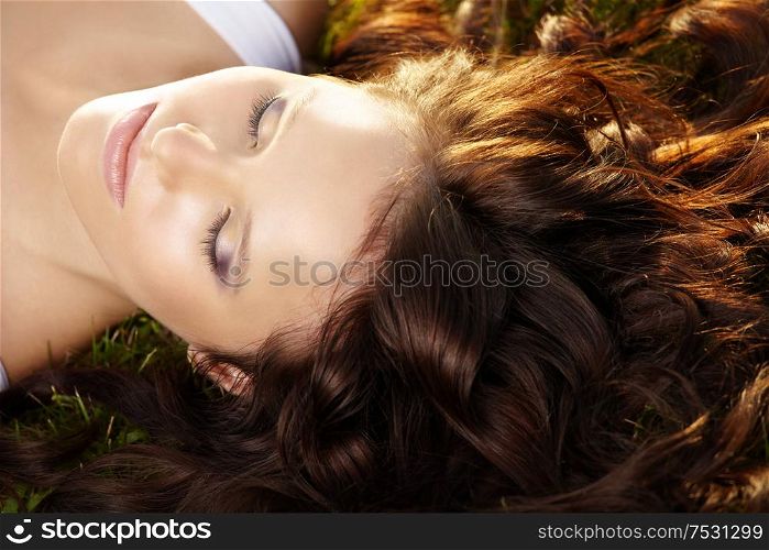 Close up of curly hair and face of beautiful girl lying on a lawn