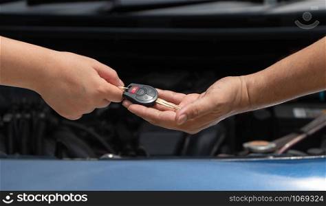 Close up of customer hand giving car key to car engine repairman on car engine background to repair it . Concept of maintenance vehicle mechanic and automotive