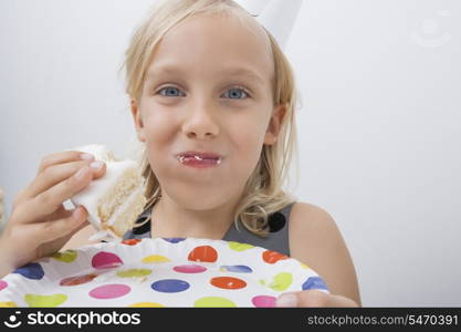 Close-up of cute girl eating birthday cake against gray background