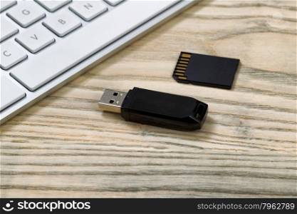 Close up of data thumb drive and memory flash card. Computer keyboard in background on desktop.