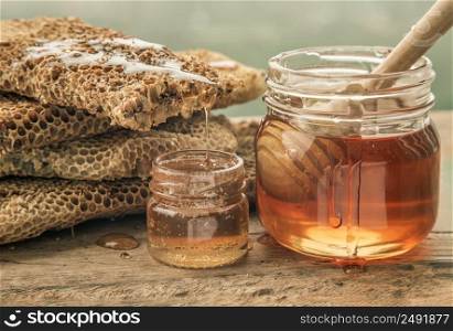 Close-up of Delicious honey dripping from Fresh honeycombs on Glass jar with Wooden honey dipper stick on old wooden table. Healthy organic natura honey, space for text, Selective focus.
