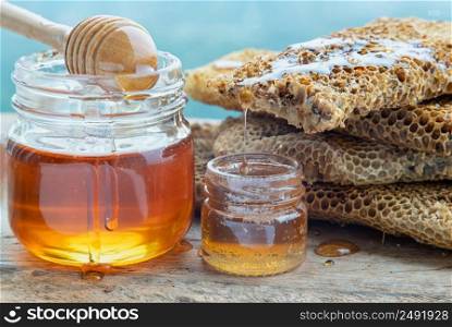 Close-up of Delicious honey dripping from Fresh honeycombs on Glass jar with Wooden honey dipper stick on old wooden table. Healthy organic natura honey, space for text, Selective focus.