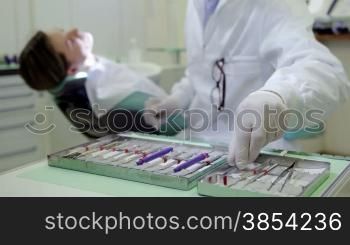 Close up of dental equipment in hospital with patient lying on exam chair and dentist working. Rack focus from tools to dentist