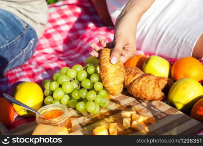 Close up of different products on the blanket prepared for picnic: fruits, croissants, berries and cheese. Products on the blanket for picnic