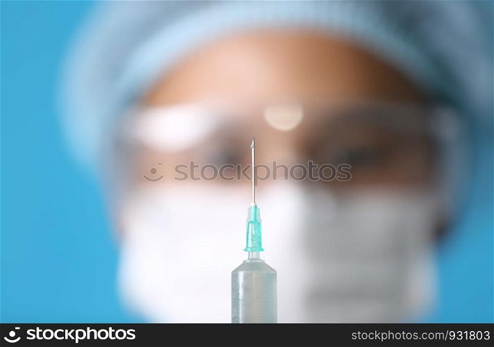 Close-Up Of doctor holding Syringe Against blue Background