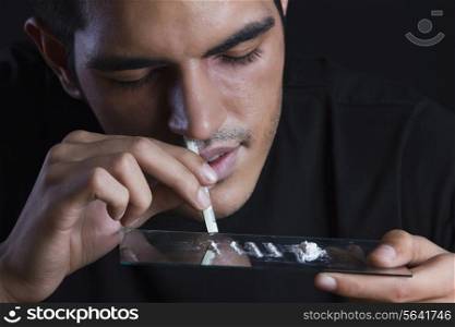 Close-up of drug addict snorting cocaine against black background