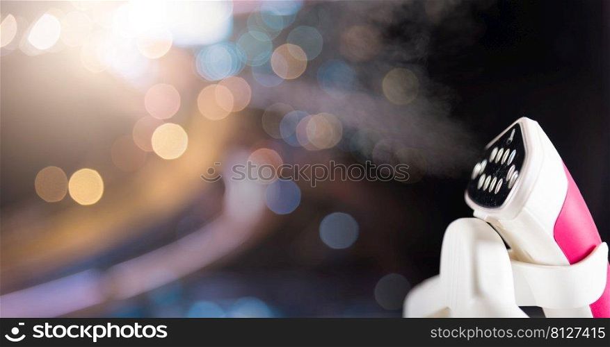 Close up of electric hand steam generator while it’s hot and steam comes out on the ironing board place for clothes on black background, Household   home equipment for housework, concept of linen care