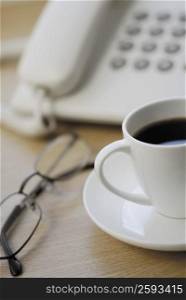 Close-up of eyeglasses and a tea cup in front of a telephone