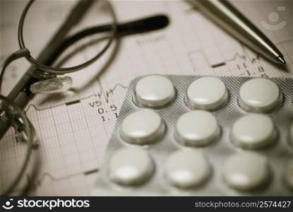 Close-up of eyeglasses with pills on an electrocardiogram report