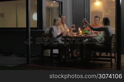 Close-up of family clinking glasses and eating dinner while sitting on veranda