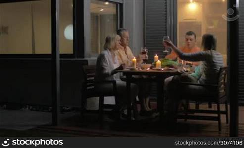 Close-up of family clinking glasses and eating dinner while sitting on veranda