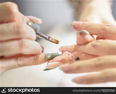 Close-up of female beautician covering woman&rsquo;s nails with nail varnish