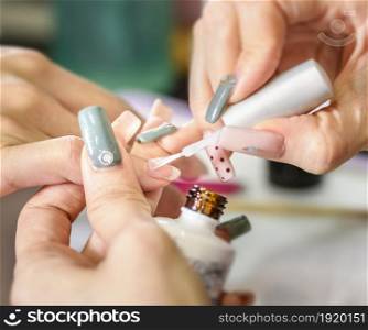 Close-up of female beautician covering woman&rsquo;s nails with nail varnish