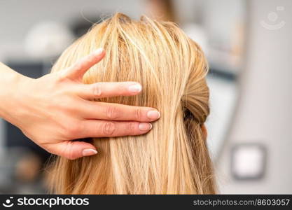 Close up of female hairdresser styling blonde hair of a young woman in a beauty salon. Female hairdresser styling blonde hair