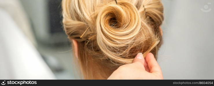 Close up of female hairdresser styling blonde hair of a young woman in a beauty salon. Female hairdresser styling blonde hair