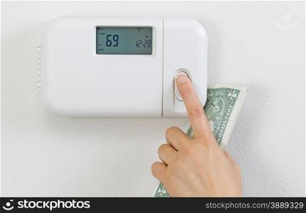 Close up of female hand adjusting home heating thermostat with partial currency money in palm.