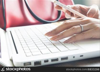 Close up of female hand using mobile phone and laptop computer, Working woman and Online Marketing concept