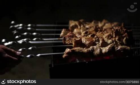 Close up of female hands cooking cubed pork kebabs on the barbecue coals outdoor at night
