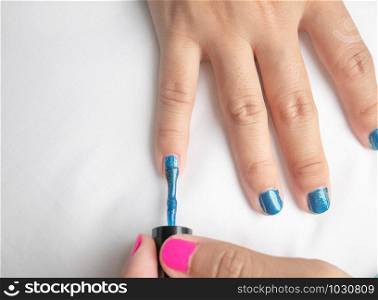 Close-up of female hands painting blue nail varnish, self made manicure at home.
