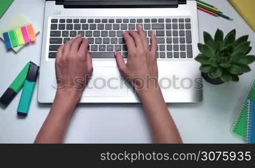 Close up of female hands typing on laptop. Woman working online on laptop on the white table with office accessories.