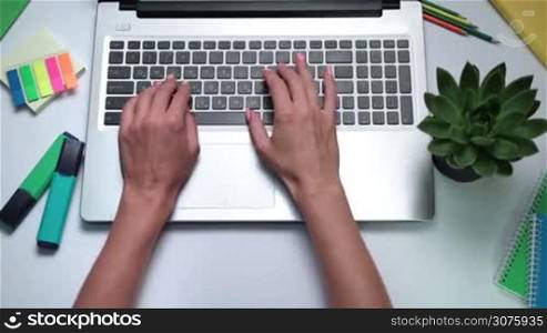 Close up of female hands typing on laptop. Woman working online on laptop on the white table with office accessories.