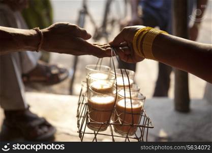 Close-up of female&rsquo;s hand passing tray of chai to man with people in background