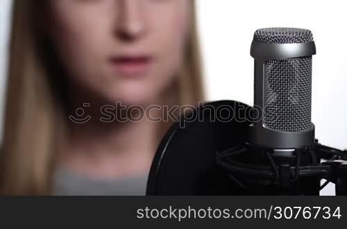 Close up of female singer recording music track in a studio. Woman recording vocals in music studio and singing with studio microphone over white background.