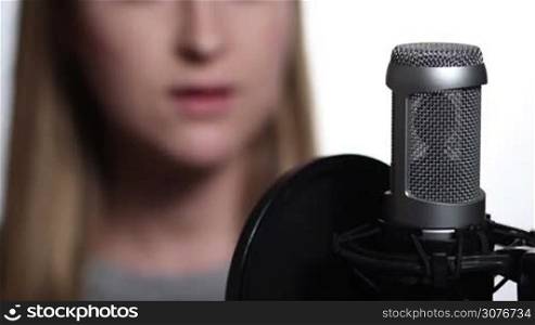 Close up of female singer recording music track in a studio. Woman recording vocals in music studio and singing with studio microphone over white background.