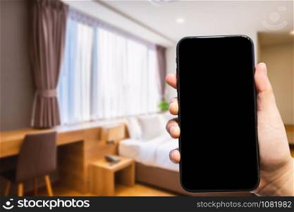 Close-up of female use Hand holding smartphone blurred images of defocused white pillow on bed decoration with light lamp in hotel bedroom interior background,Leisure and travel in the holiday concept