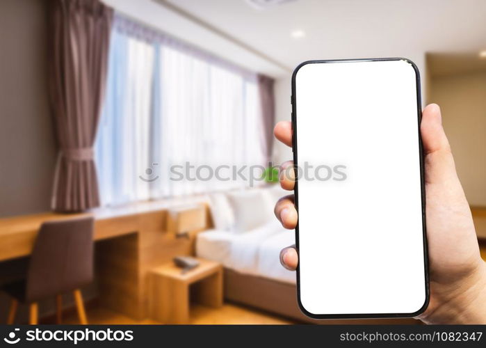 Close-up of female use Hand holding smartphone blurred images of defocused white pillow on bed decoration with light lamp in hotel bedroom interior background,Leisure and travel in the holiday concept