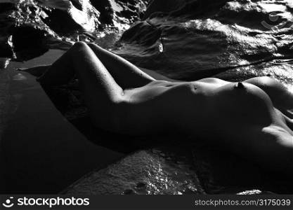 Close up of Filipino young nude woman lying on back in water on rocky beach.