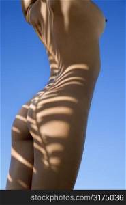 Close up of Filipino young nude woman standing against blue sky with sun streaks on body.