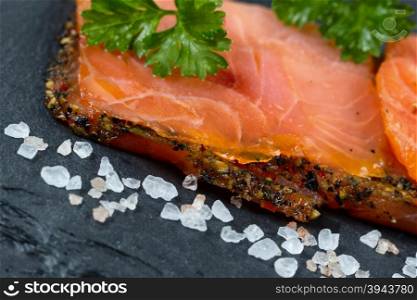 Close up of finely sliced smoked salmon, tilted angle, on natural slate stone with coarse salt. Selective focus on front part of salmon.