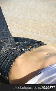Close up of fit Caucasian woman&acute;s midriff area wearing low rise blue jeans on beach.