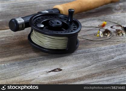 Close up of fly reel, focus on front bottom of reel, with partial cork handled pole and flies blurred out on rustic wooden boards &#xA;&#xA;
