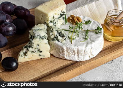 Close up of french cheeses assortment. Delicatessen camembert, brie, and roquefort with honey and grapes.