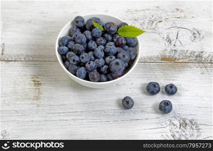 Close up of fresh blueberries, inside and outside of bowl, on rustic white wooden table.